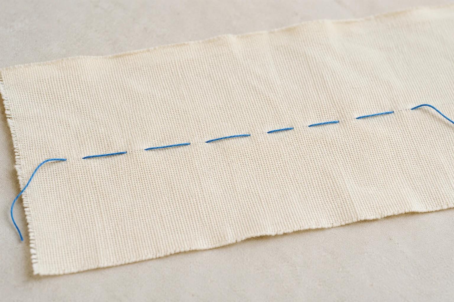 Long temporary basting stitches sewn in contrasting thread across pale woven fabric