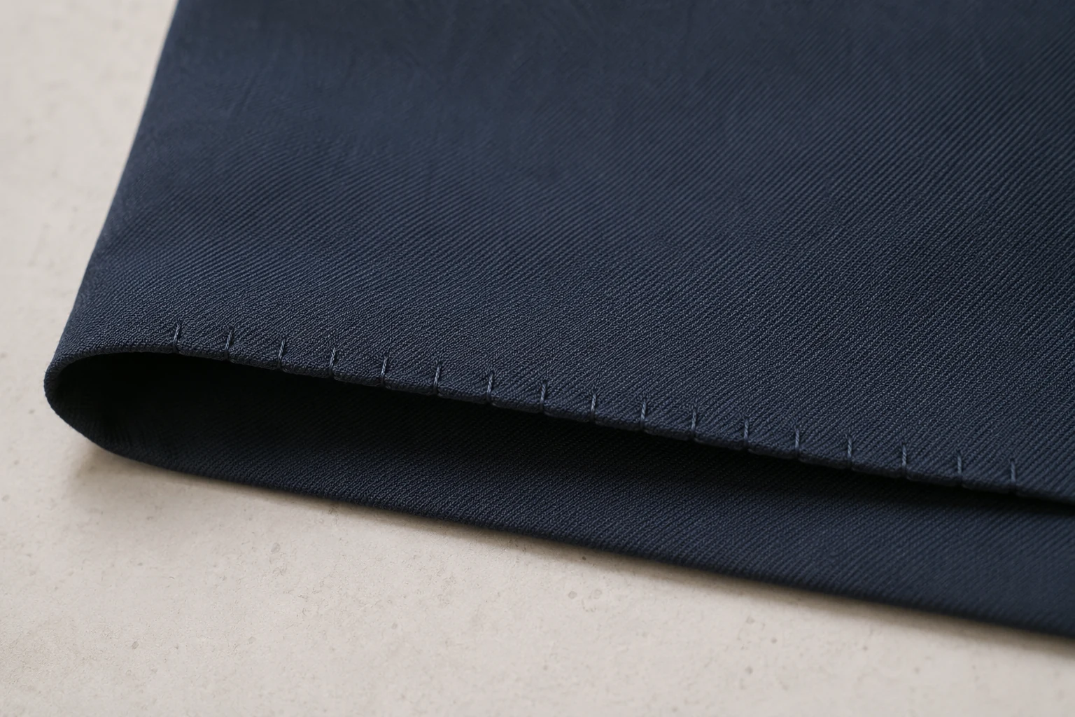 Folded navy fabric hem showing small widely spaced blind-hem catches along the edge