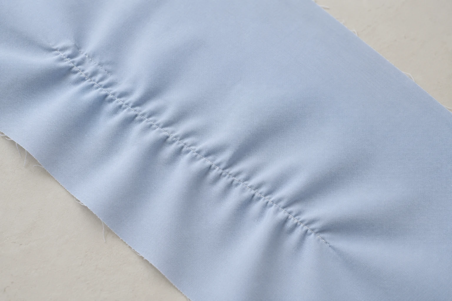 Stitched seam on pale blue fabric showing visible ripples and puckering beside the thread line