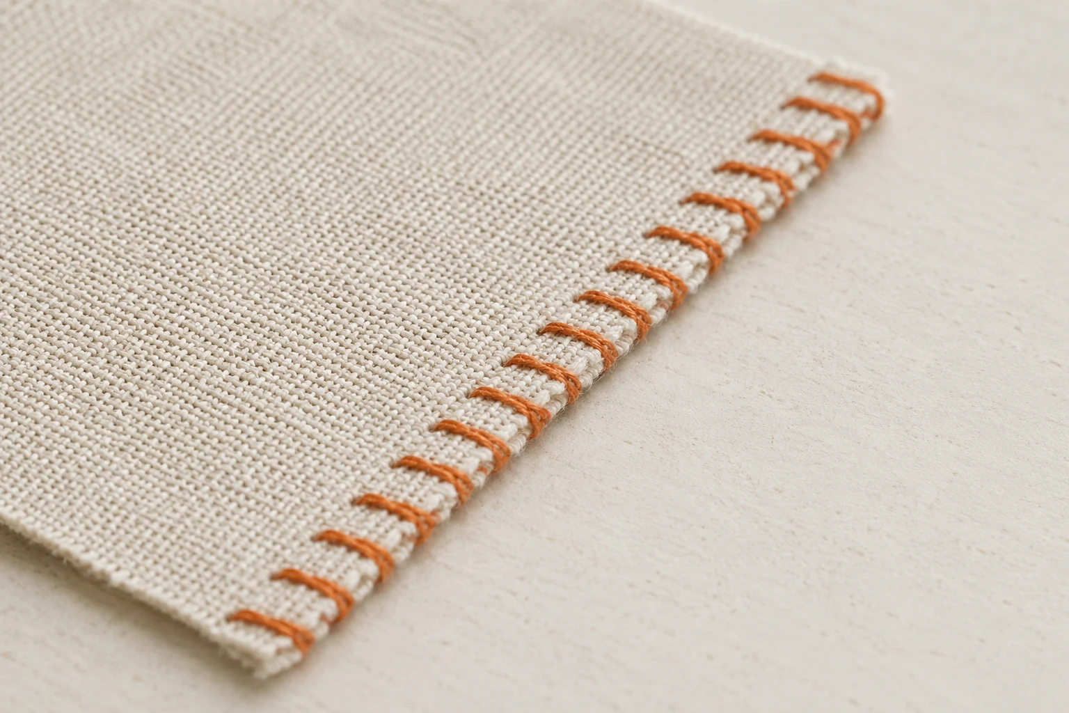 Orange overcast stitches wrapping the raw edge of beige woven fabric to control fraying