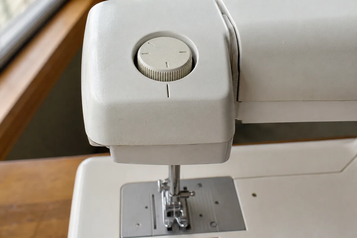 Top-mounted presser-foot pressure adjustment dial on a domestic sewing machine