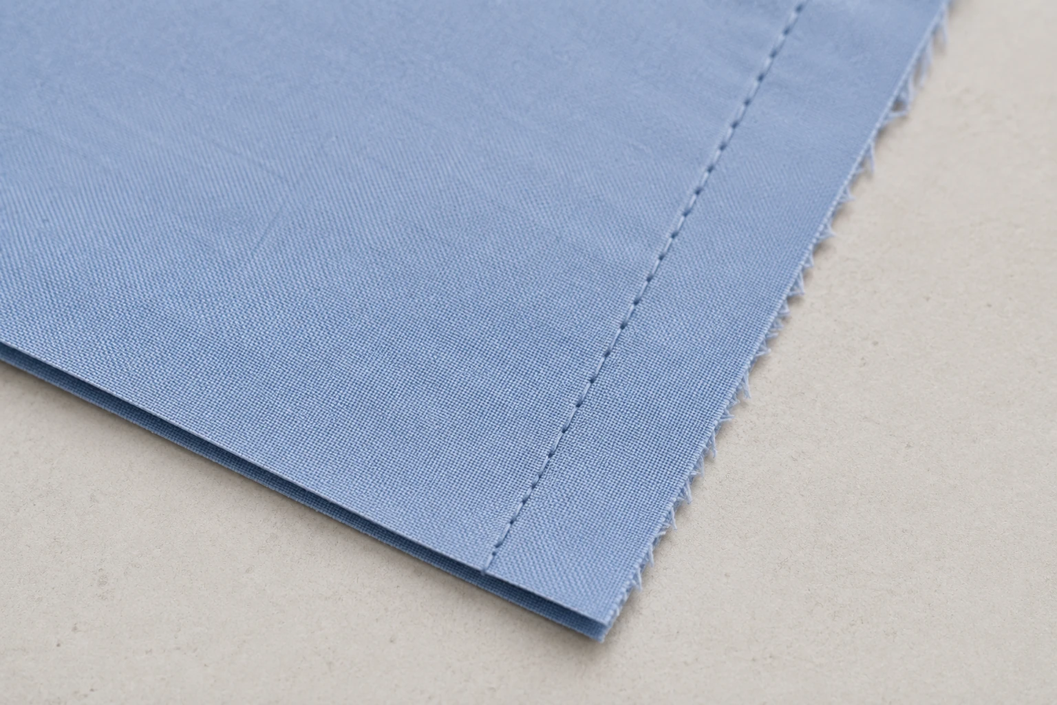 Straight seam on blue fabric showing the space between the stitch line and raw edge