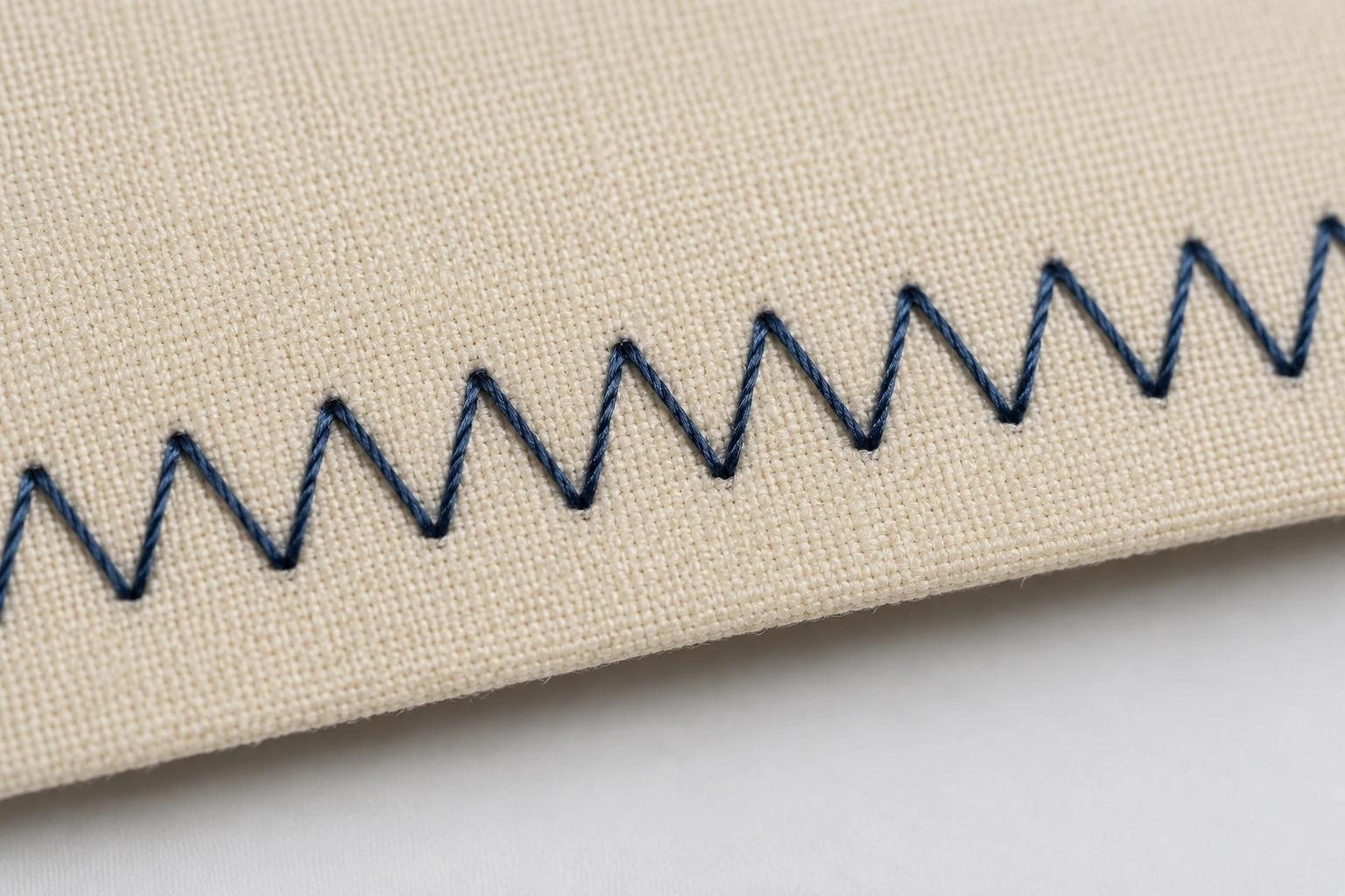 Even navy zigzag stitch sewn across cream woven fabric